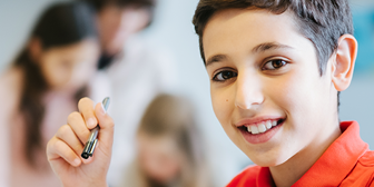 Mörkhårig kille ler mot kameran. Två andra barn i bakgrunden