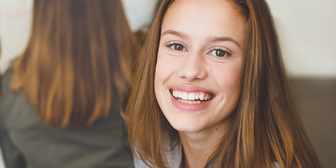 Tjej med långt brunt hår ler mot kameran