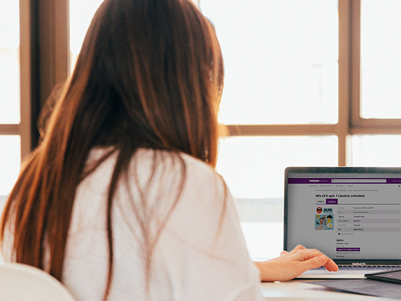 Kvinna med brunt hår sedd bakifrån, sitter framför en laptop