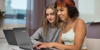 Två unga flickor sitter i ett klassrum framför en laptop