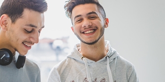 Två unga män, ena ler mot kameran och den andra har hörlurar runt halsen och kollar ned