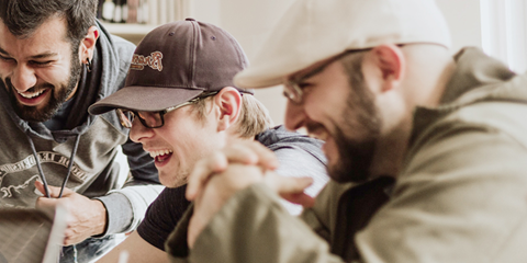 Tre killar skrattar framför en laptop