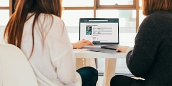 Kvinna med brunt hår sedd bakifrån, sitter framför en laptop