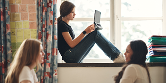 En tjej sitter med en laptop i ett fönster. 