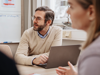 En lärare sitter vid en bärbar dator. En annan lärare sitter mitt emot honom.