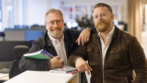 Två kundansvariga står och håller upp Sanomas böcker i ett kontorslandskap.